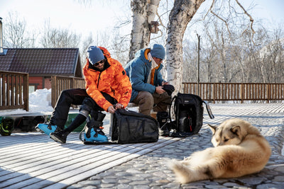 Skiers pulling ski boots out of EVOC gear bags while sitting out on a cold deck
