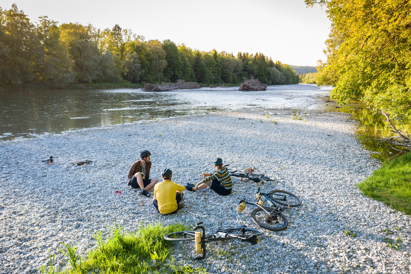 EVOC gravel bike riders with bike packing bags sitting next to Isar River in Germany