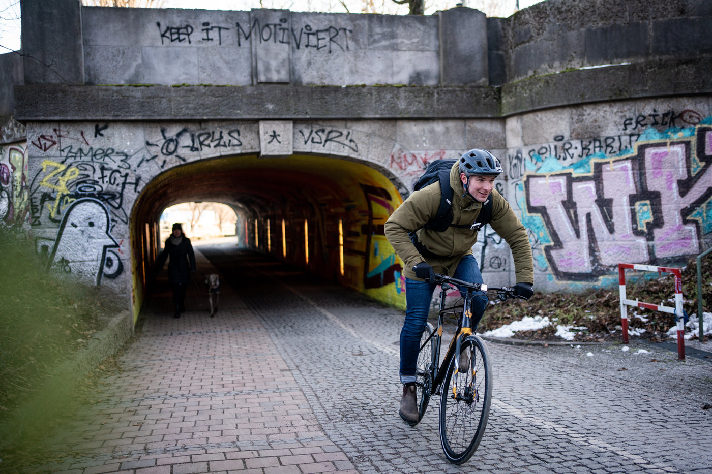 Bike commuter wearing EVOC backpack while riding out from under a bridge on a cobbled bike path