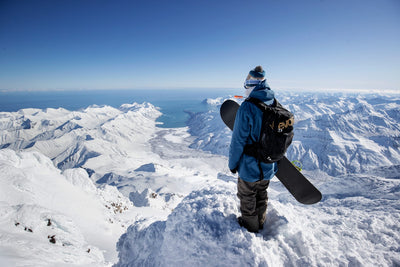 Snowboarder wearing EVOC snow backpack standing atop wintery peak