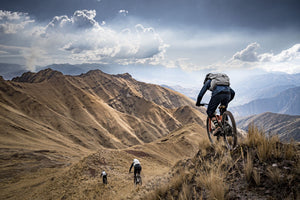Mountain bikers wearing EVOC backpacks descending grassy ridge in Peru