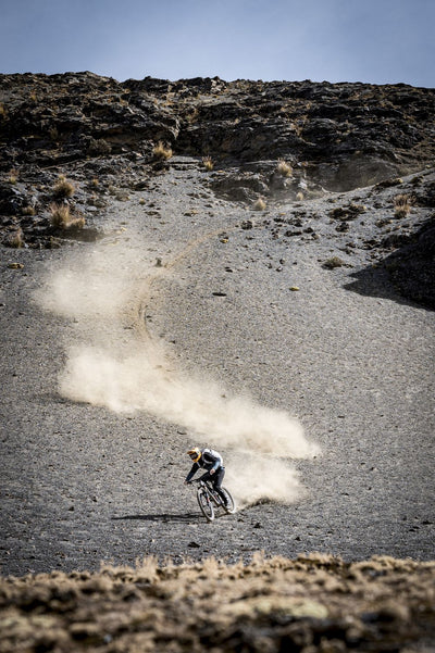 Dust billowing up behind mountain biker riding down talus slope