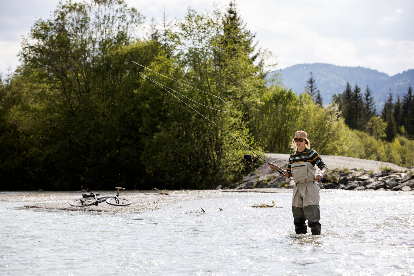 Woman fly fishing Isar River in Germany with EVOC equipped gravel bike in the background