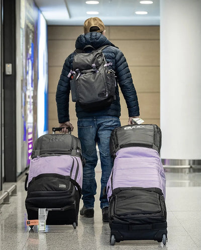 EVOC Snow Gear Roller and World Traveller luggage being rolled through an airport by a man wearing an EVOC backpack