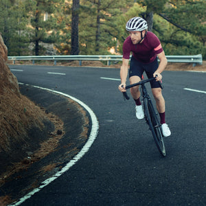 EVOC athlete cycling up a black asphalt mountain road with pine trees in the background mobile view