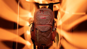 EVOC Explorer 30 liter backpack backlit hanging in front of louvered shutters letting in filtered sunlight